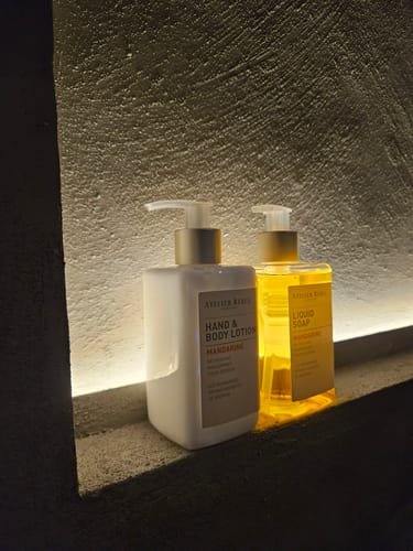 De Mandarine Handzeep van een klant naast de bijpassende lotion, sfeervol verlicht op een richel.