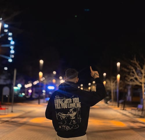 Reviewer from behind wearing the black "TILL YOU LOVE ME" vintage hoodie, showing the large back graphic on a street at night.