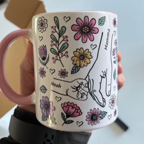 Kundens Kärleksmugg med en personlig illustration av händer, namnen 'Mamma' och 'Noah' och ett blommigt mönster.