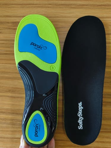 Reviewer holds the Ortho Support Insole, showing its green and black supportive base next to a standard black insole.