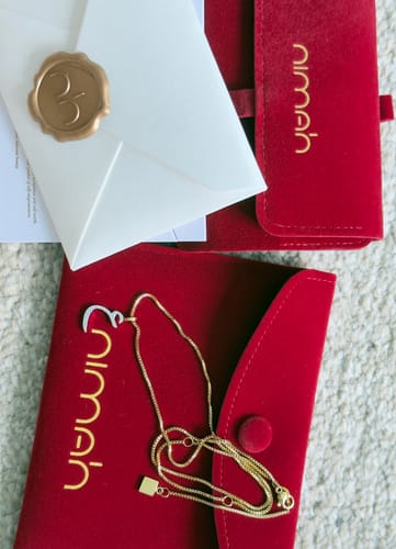 Customer's Pavé Letter Necklace on its red velvet pouch next to a sealed envelope and second pouch.