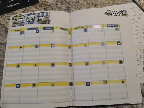 Customer's bullet journal with a May calendar spread decorated with cute llama market stall stickers from the Journal Subscription.