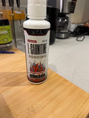 Customer's white bottle of Liquid L-Carnitine 4000MG, Sour Gummy Worms flavor, on a wooden kitchen counter.