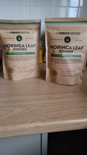 Customer's two pouches of Organic Moringa Leaf Powder standing on a wooden kitchen counter.