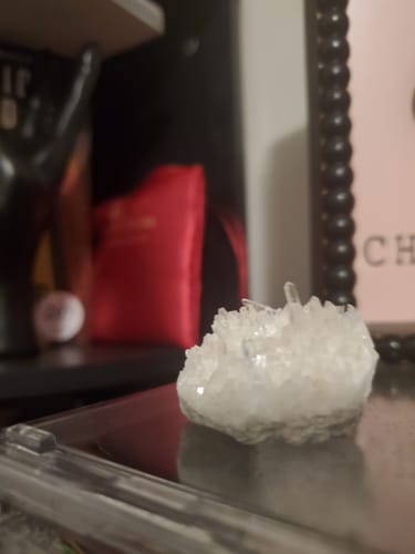 Reviewer's close-up of a small clear quartz cluster sitting on a dark, reflective surface.