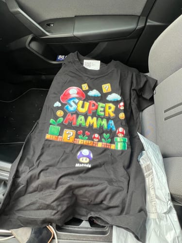 Ein Kunde zeigt das personalisierte schwarze T-Shirt "Super Mamma" auf einem Autositz.