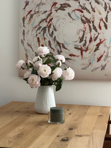 Recensent toont de lichtroze Zijden Pioenrozen in een witte vaas op een houten tafel.