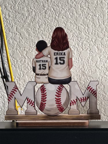 Customer's personalized wooden plaque with a mom and son in custom jerseys sitting on the word 'MOM' with a baseball.