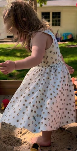 Customer's daughter wearing a white printed dress with a full skirt from the grab bag in a sandbox.