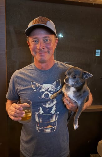 Customer wearing the Whiskey Dog Chihuahua t-shirt holds a real chihuahua and a glass of whiskey.
