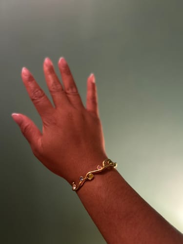 Customer wearing the gold Estelle Crystal Adjustable Cuff with multi-colored crystals on their wrist.