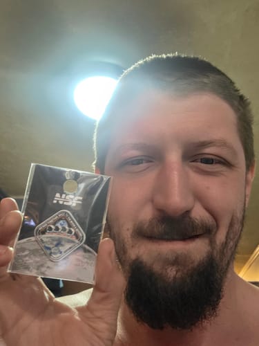 A smiling reviewer holds up the Artemis II Collectors Pin, still in its packaging with the NSF-branded header card.