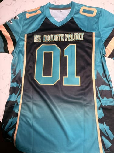 Customer's custom football jersey in vibrant teal and black, showing 'THE MEGABETH PROJECT' and number '01' on the front.
