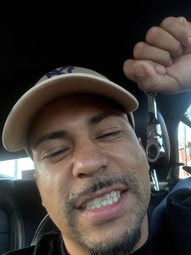Reviewer smiling in their car while holding up the 10mm Wrench Keychain.