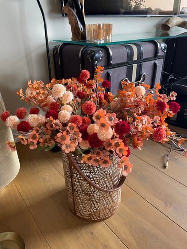 Klant toont het Wax Arrangement - Mix als een vol, dubbel boeket in tinten van rood en oranje.