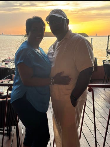Customer and a companion posing for a photo on a patio overlooking the water at sunset.