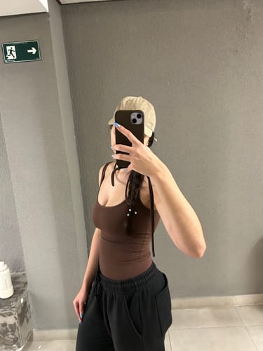 Cliente tirando uma selfie no espelho, mostrando a case Odara Marrom Café com sua alça transversal.