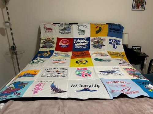 Customer's large Project Repat T-Shirt Quilt made from colorful racing t-shirts, spread across a bed.