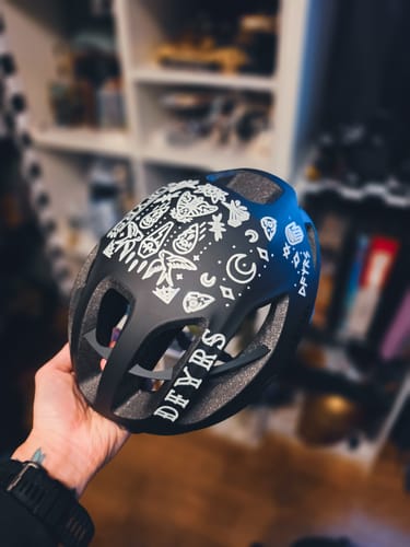 A customer's hand holding a black bike helmet decorated with white Occult Transfer Decals.