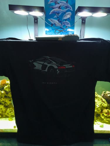 Customer's black 80Eighty DCG88 shirt with a white sports car graphic held up in front of an aquarium.