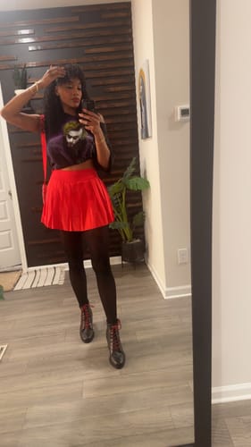 Customer taking a mirror selfie, wearing the Batman Character Tee cropped with a red skirt and black tights.