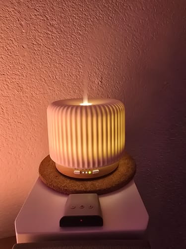 Recensent toont de verlichte, keramische Live Slow Aroma Diffuser die nevel verspreidt.