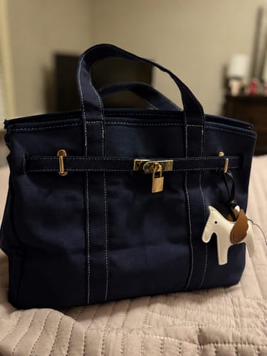 Customer's navy blue Boatkin Bag with gold hardware and a decorative lock, sitting on a bed.