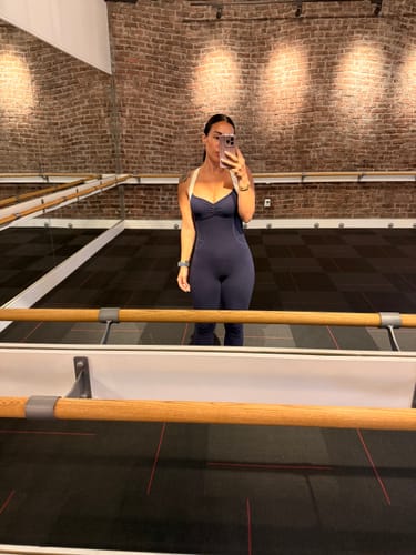 Customer taking a full-length mirror selfie in the navy Sculpt Onesie in a studio.