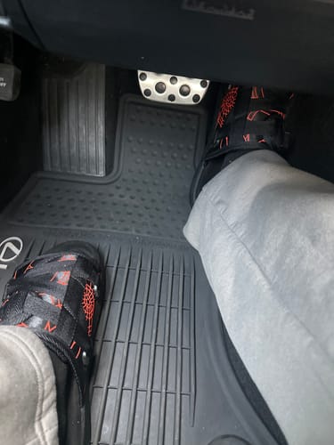 A customer wearing black Mystery DracoSlides with a red pattern in the driver's footwell of a car.