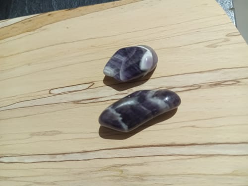 Client montrant deux pierres d'améthyste polies, violettes et blanches, sur une surface en bois clair.