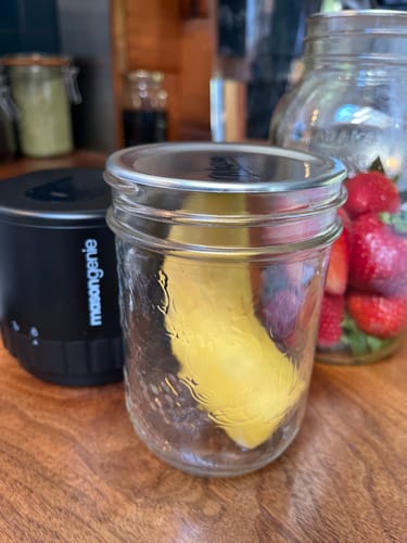 Customer's black Mason Genie vacuum sealer next to a mason jar with a sealed half banana on a wooden counter.