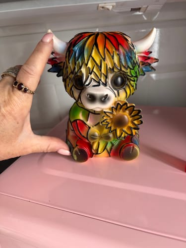 Customer showing the small size of the colorful Highland Cow figurine with their hand.