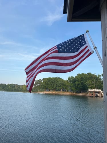 Customer's Ultra Heavy Duty American Flag waving on a pole over a lake, with trees in the background.