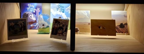Customer's 'On the Way to Meet Mom' manhwa and merchandise collection displayed on a lit wooden shelf.