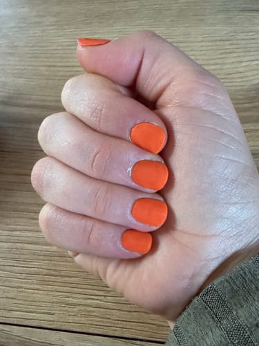 Nahaufnahme der Hand eines Kunden, die die orangefarbenen 'Tempting Tangerine' UV-Gel-Folien auf kurzen Nägeln zeigt.