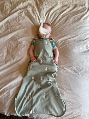 Customer's baby lying on a bed in the long, goose-patterned Ultimate Baby Sleep Bag.