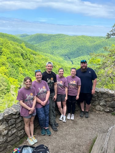 A group of reviewers wear matching purple Out Of Breath T-shirts on a mountain overlook.