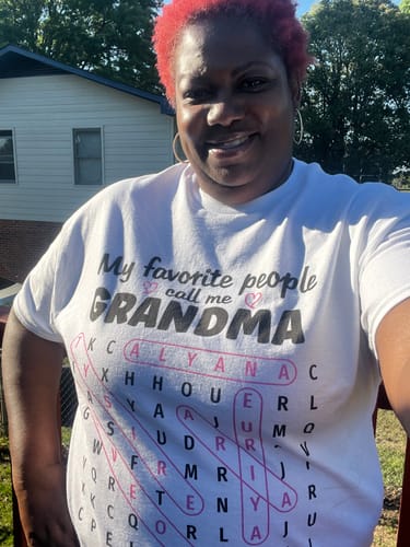 Reviewer smiling while wearing the white personalized Grandma's Favorite People word search shirt outdoors.