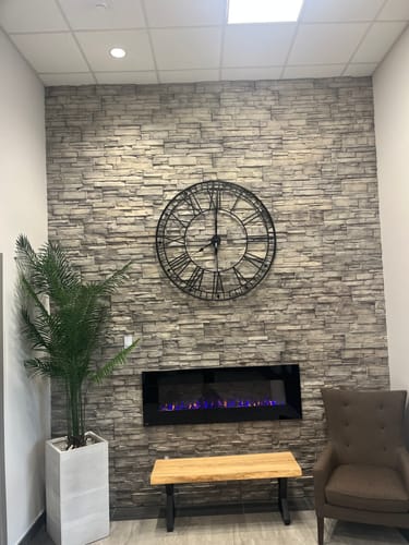 Customer's 48" black Roman numeral wall clock mounted on a stylish stone wall in an apartment entrance.