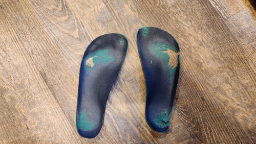 Customer's old, worn-out barefoot shoe insoles showing heavy wear patterns on a wood floor.