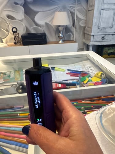 Reviewer holding the purple Al Fakher Crown Bar disposable vape, showing its lit digital screen with the battery level.