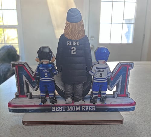 Customer's personalized wooden plaque showing a hockey mom and two kids with custom names, on a base reading 'BEST MOM EVER'.