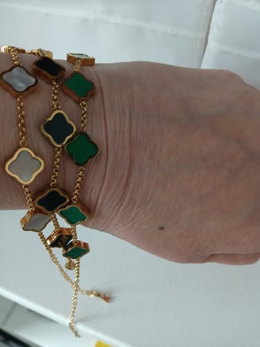 Reviewer's wrist showing three layered Celine Clover Bracelets with white, black, and green charms.