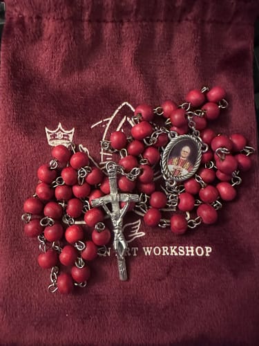 Customer's Pope Leo XIV Rosary with rich red wood beads displayed on a dark red pouch.