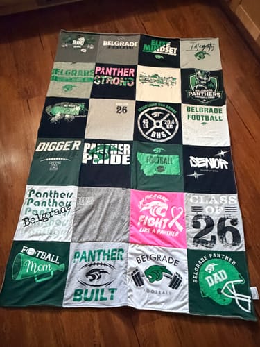 Customer's Project Repat T-Shirt Quilt made with their son's green and white football-themed shirts, laid out on a wood floor.