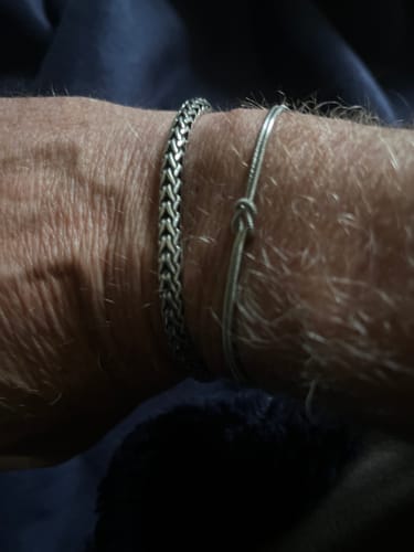 Customer's wrist wearing a thick woven silver bracelet and a thin knotted silver bracelet.