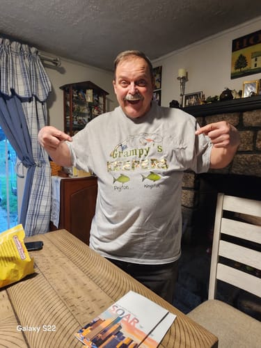 Customer happily pointing to the personalized design on their gray Grandpa's Keepers fishing shirt.