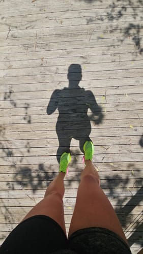 Reviewer's point-of-view shot of their bright neon green Flame 5 "Redline" running shoes on a wooden deck.