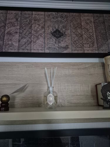 Rezensent zeigt den magischen Raumduft auf einem Regal, platziert vor einem mystischen Bild.