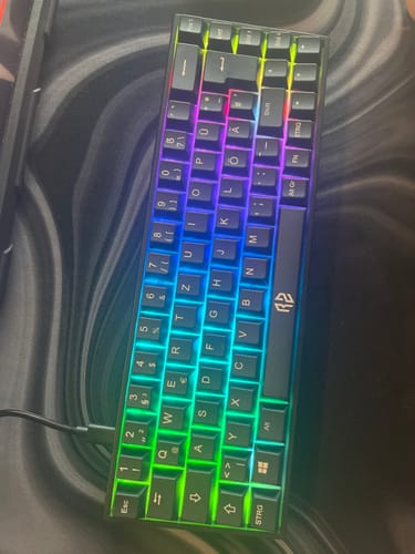 Ein Rezensent zeigt die schwarze RZ Gaming-Tastatur RZ 65 HE mit leuchtender, bunter RGB-Beleuchtung.